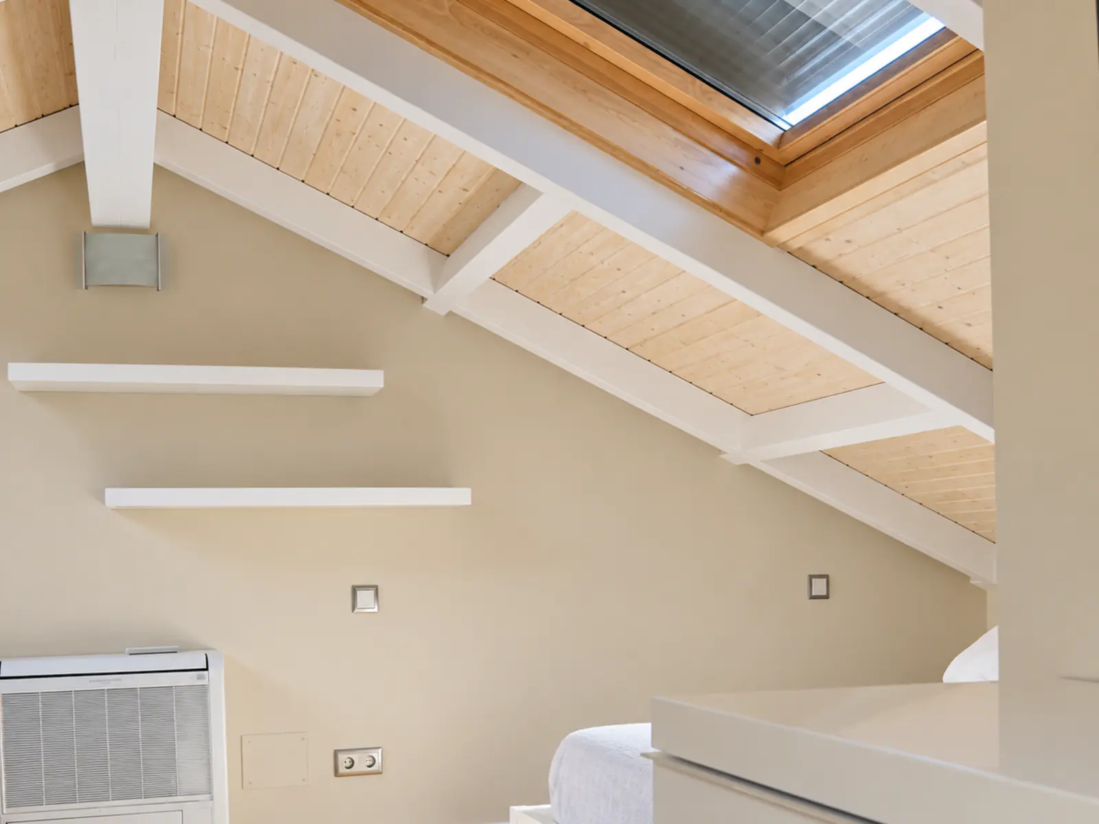 Vivienda rehabilitada con estructura de cubierta de vigas blancas, madera y ventana de tejado