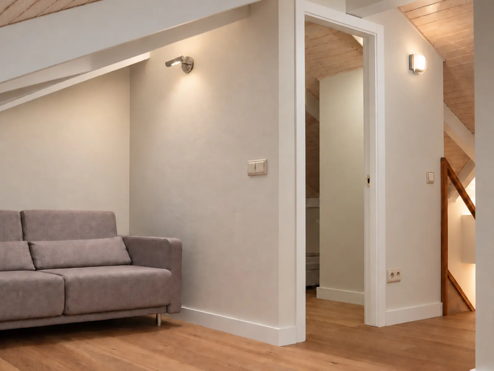 Zona de estar de la vivienda rehabilitada, con sofá, suelo de madera y paso hacia otra estancia